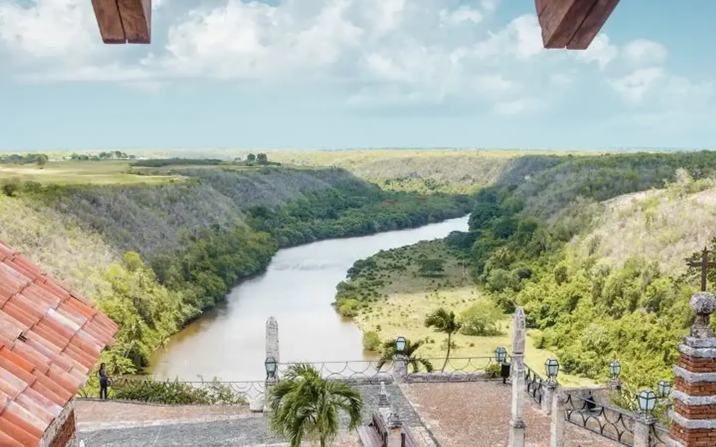 A panoramic view from a tiled roof overlooks a winding river through a lush, green canyon under a cloudy sky.